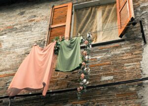 Waschen auf Reisen: Frauenkleider auf einer Wäscheleine außen am offenen Fenster. Bild: phio-pixabay