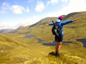 Eine Wandersfrau steht mit einem gut gepackten Wanderrucksack an einem Aussichtspunkt auf der Isle of Skye. Bild: WomenFairTravel